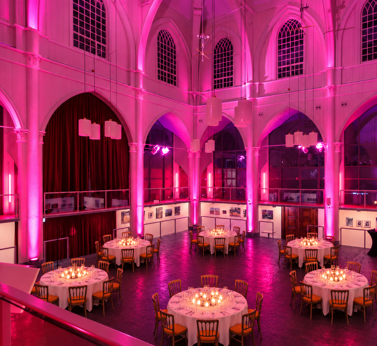 Sfeerimpressie van ronde gedekte dinertafels in de roze verlichte Amstelkerk